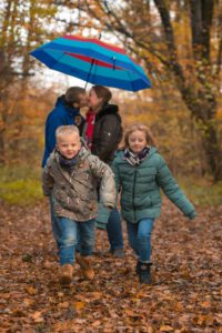 Kids laufen zur kamera. Eltern küssen unter Schirm