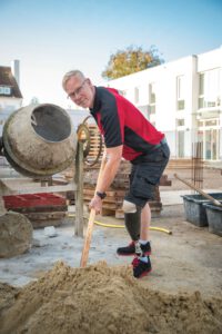 Mann bei körperlicher Arbeit auf der Baustelle mit Orthese. Image Kampagne für lokales Unternehmen